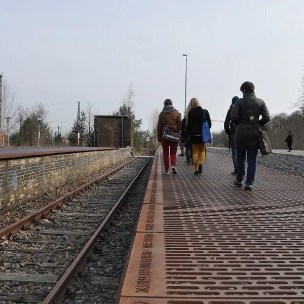 Junge Menschen laufen am Bahnsteig des Mahnmal Gleis 17 am Bahnhof Grunewald entlang. 