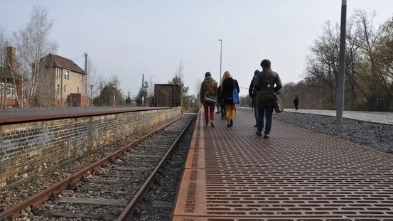 Junge Menschen laufen am Bahnsteig des Mahnmal Gleis 17 am Bahnhof Grunewald entlang. 