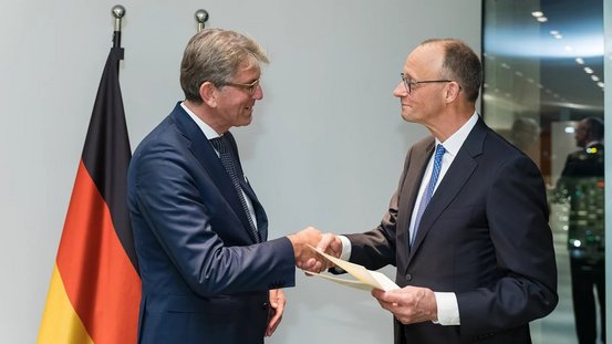 Bundeskanzler Friedrich Merz reicht Wolfram Weimar die Hand und reicht ihm seine Urkunde aus. 