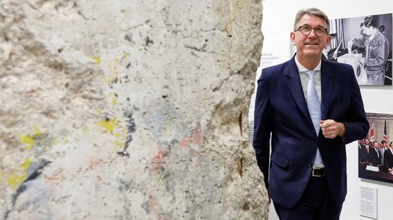 Staatsminister Weimer geht in der Ausstellung in M&ouml;dlareuth an einem St&uuml;ck der Mauer entlang