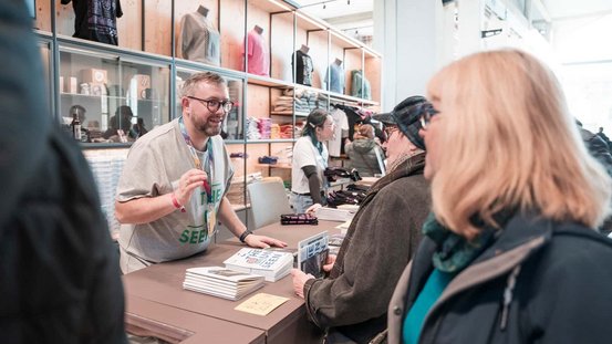 Ein Mitarbeiter berät Besucherinnen im Besuchs- und Informationszentrum zum Kulturhauptstadtprogramm.