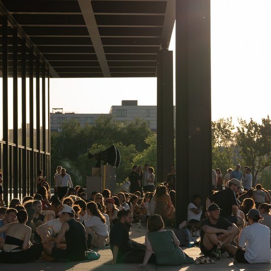 Besucherinnen und Besucher sitzen vor der Nationalgalerie in der Abendsonne 