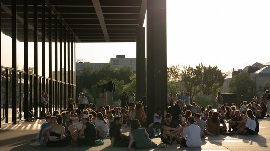 Besucherinnen und Besucher sitzen vor der Nationalgalerie in der Abendsonne 