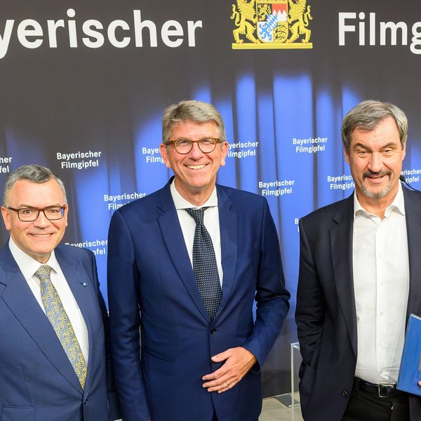 Staatskanzleiminister Florian Herrmann, Kulturstaatsminister Wolfram Weimer und Ministerpräsident Markus Söder stehen in der Bayerischen Staatskanzlei vor einer Wand mit der Aufschrift "Bayerischer Filmgipfel".