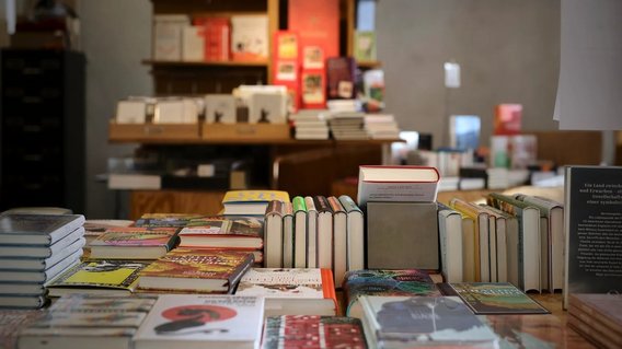 B&uuml;cher liegen auf einem Pr&auml;setiertisch in einer Buchhandlung, im Hintergrund sind B&uuml;cherregale zu sehen. 
