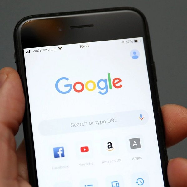 Person hält ein Handy in der Hand, auf dessen Bildschirm Apps wie Google und Facebook zu sehen sind. 