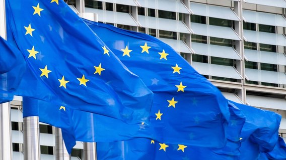 Europ&auml;ische Flaggen an Masten vor einem Geb&auml;ude.