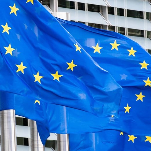 Europ&auml;ische Flaggen an Masten vor einem Geb&auml;ude.