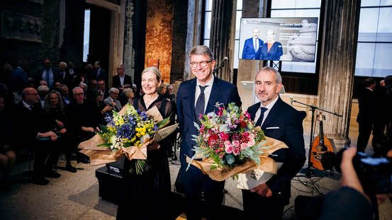 Foto von Kulturstaatsminister Weimer mit Marion Ackermann und Hermann Parzinger. Ackermann und Parzinger halten Blumensträuße in der Hand.