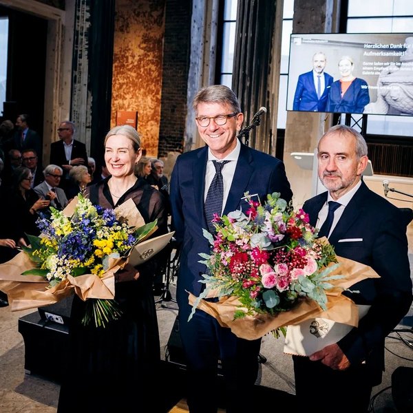 Foto von Kulturstaatsminister Weimer mit Marion Ackermann und Hermann Parzinger. Ackermann und Parzinger halten Blumensträuße in der Hand.
