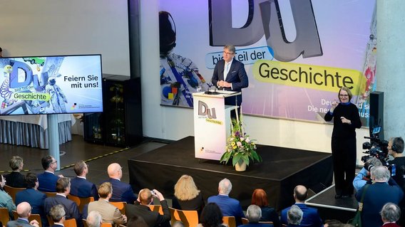 Staatsminister h&auml;lt am Rednerpult auf der B&uuml;hne eine Festansprache.