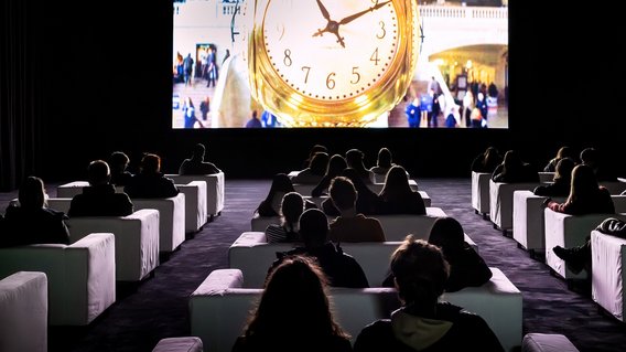 Blick auf die Installation "The Clock" in dunklem Raum in der Neuen Nationalgalerie. 