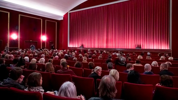 Zuschauerinnen und Zuschauer schauen im vollen Kinosaal auf die Leinwand.